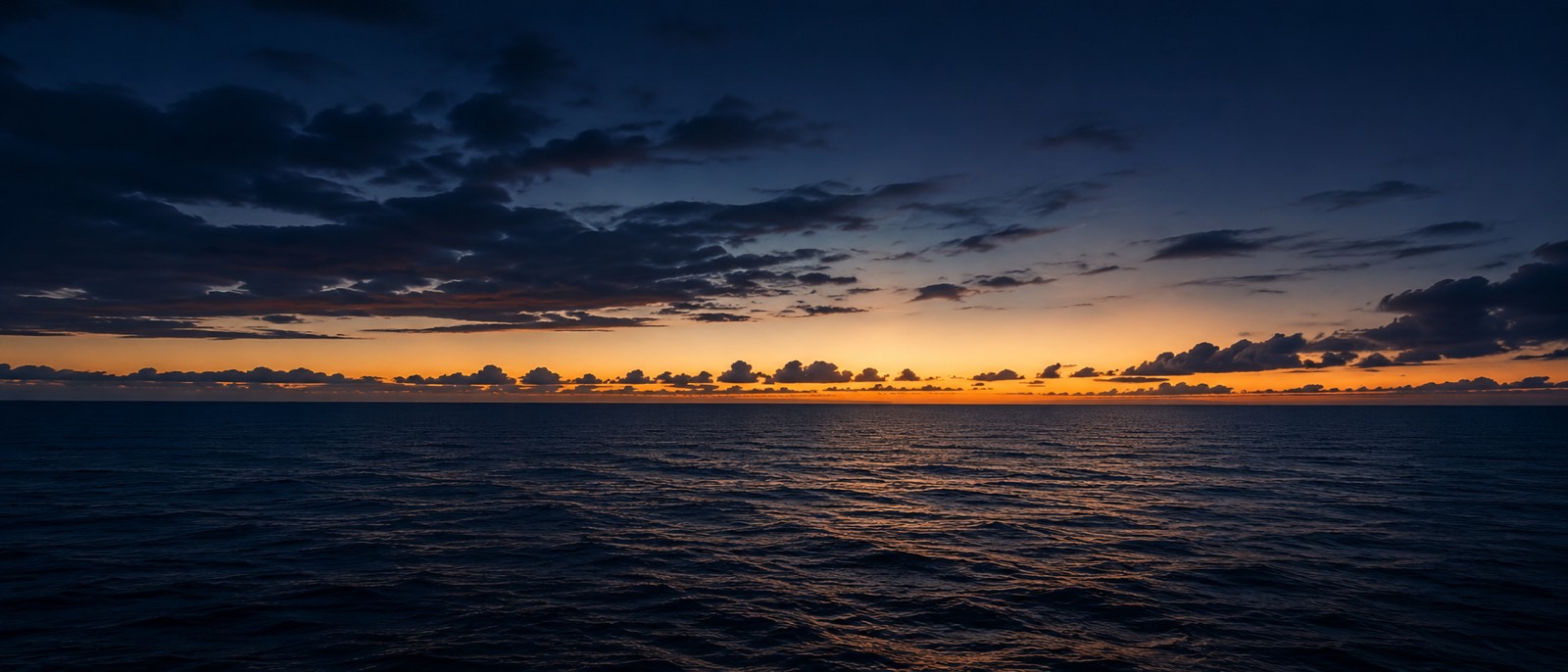 Mar aberto ao entardecer, em tons de azul profundo com horizonte dourado