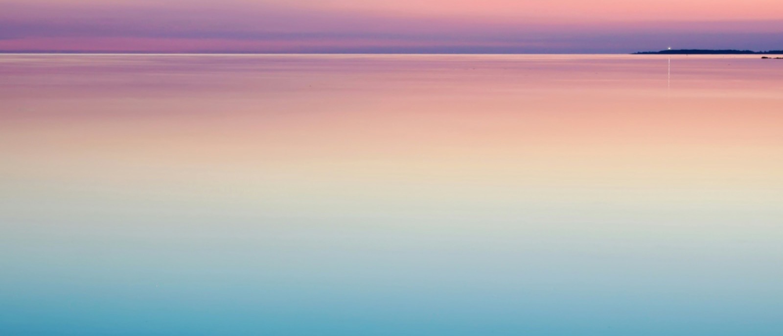 Mar completamente calmo ao entardecer, em degradê de rosa e azul